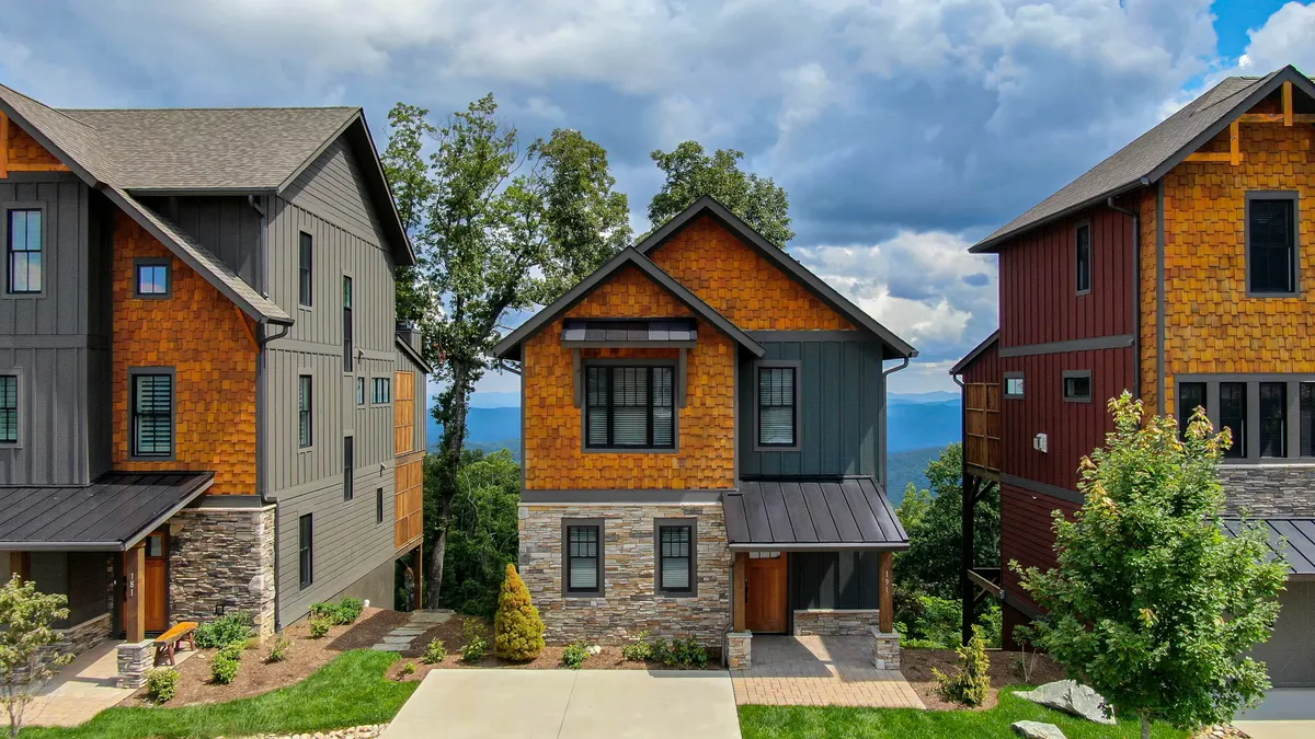 The image showcases a beautifully designed single-family house with warm wood and stone accents, set against a breathtaking mountain backdrop. The covered porch features an inviting gas fireplace, perfect for outdoor gatherings, with scenic views stretching into the distance. The setting evokes tranquility, with the promise of vibrant sunsets and serene mountain evenings.