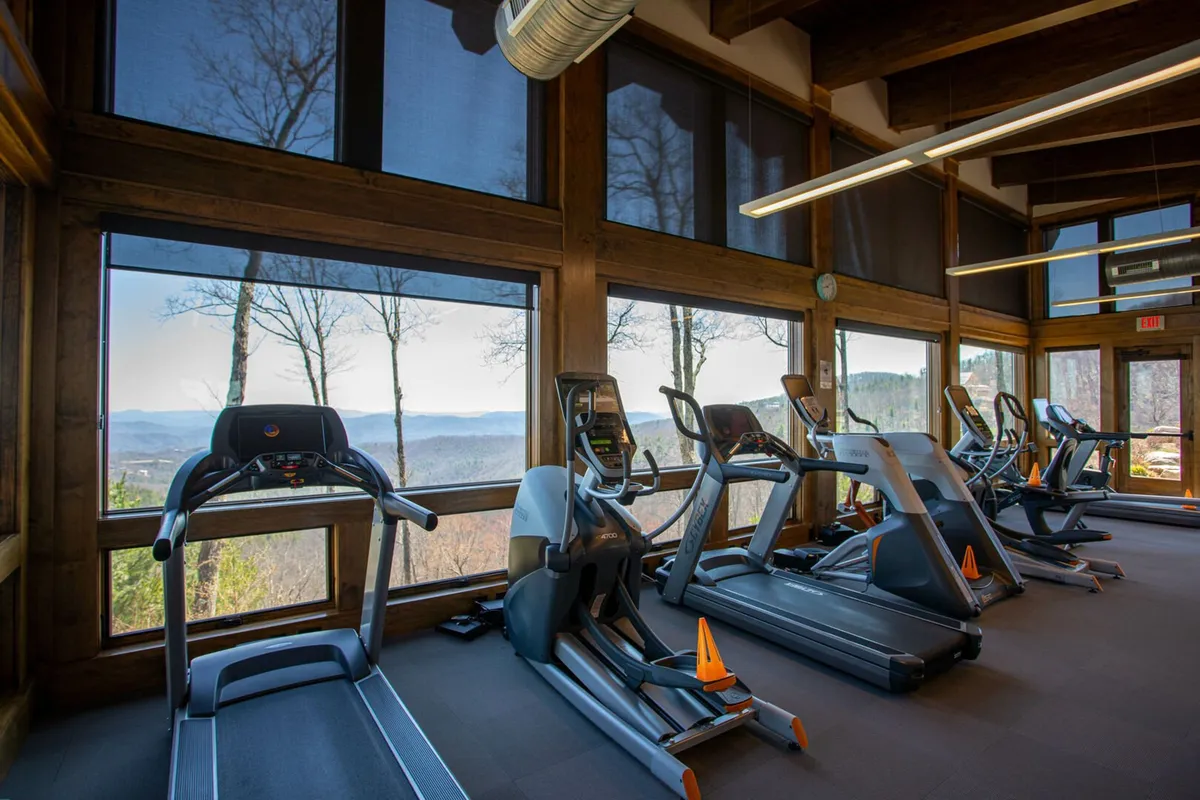 A bright, modern fitness center with treadmills positioned in front of expansive windows, framing sweeping mountain vistas. The space is filled with natural light, encouraging both solo and group workouts, yoga, and meditation.