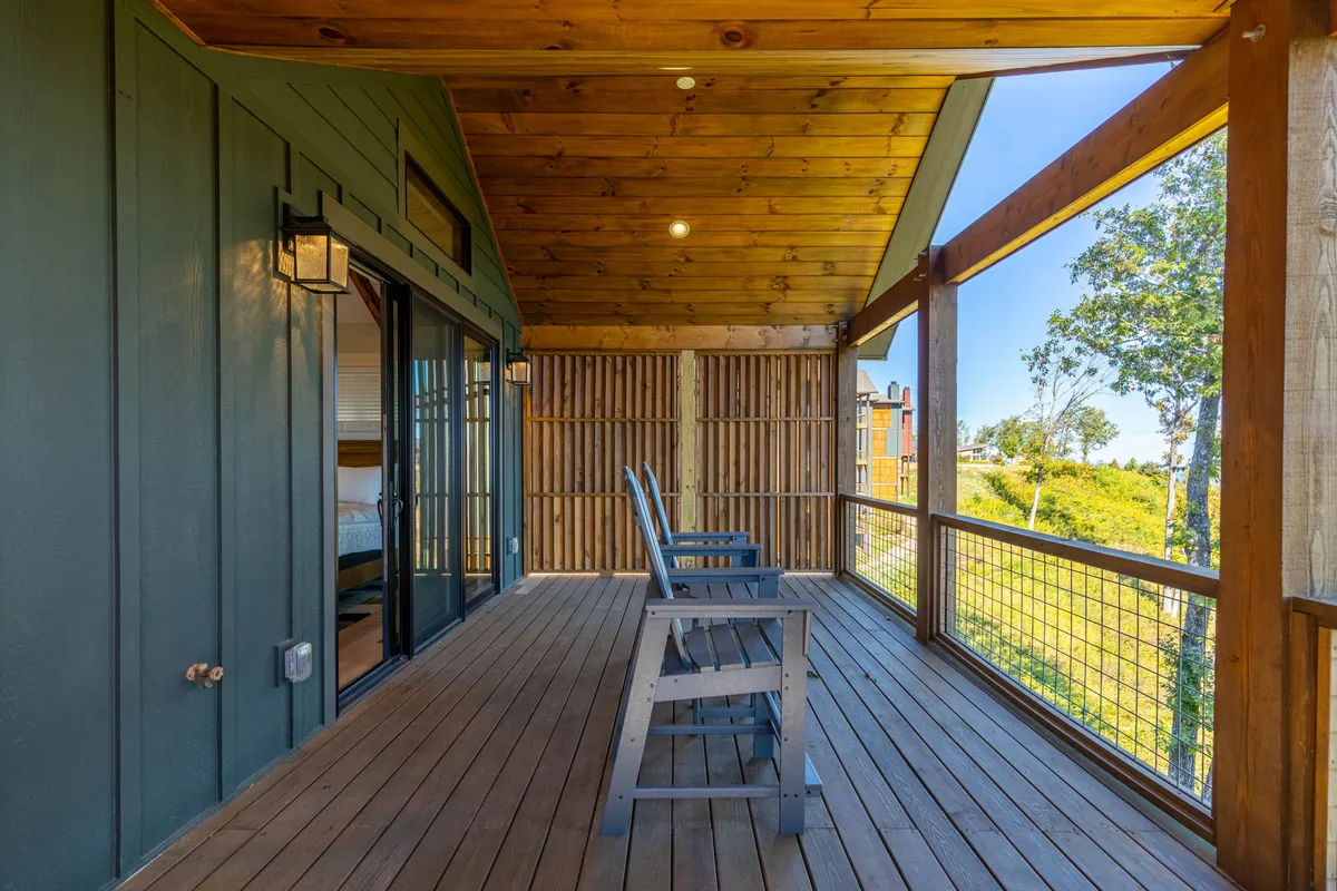 The image features a tranquil porch with rustic wooden rocking chairs, a wooden ceiling, and glass doors leading to the home's interior. Surrounded by lush greenery, the scene evokes a sense of peaceful solitude and luxurious comfort—perfect for enjoying coffee or unwinding with a view.
