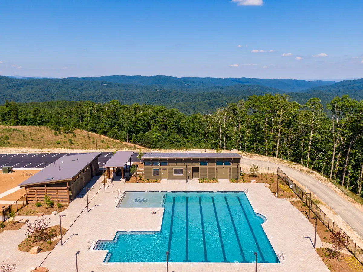 An expansive outdoor pool area bordered by plush lounge seating and surrounded by majestic mountain scenery. The setting invites relaxation, sunbathing, and vibrant social gatherings, illustrating the club's seasonal vibrancy.
