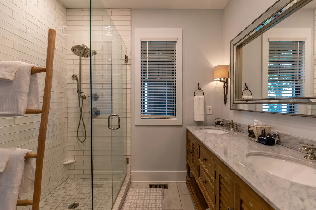 The image displays a spa-like bathroom with a glass shower enclosure, a double vanity with a marble countertop, and a wooden towel ladder. The serene and inviting mood, along with the modern fixtures, convey a spa-inspired experience.