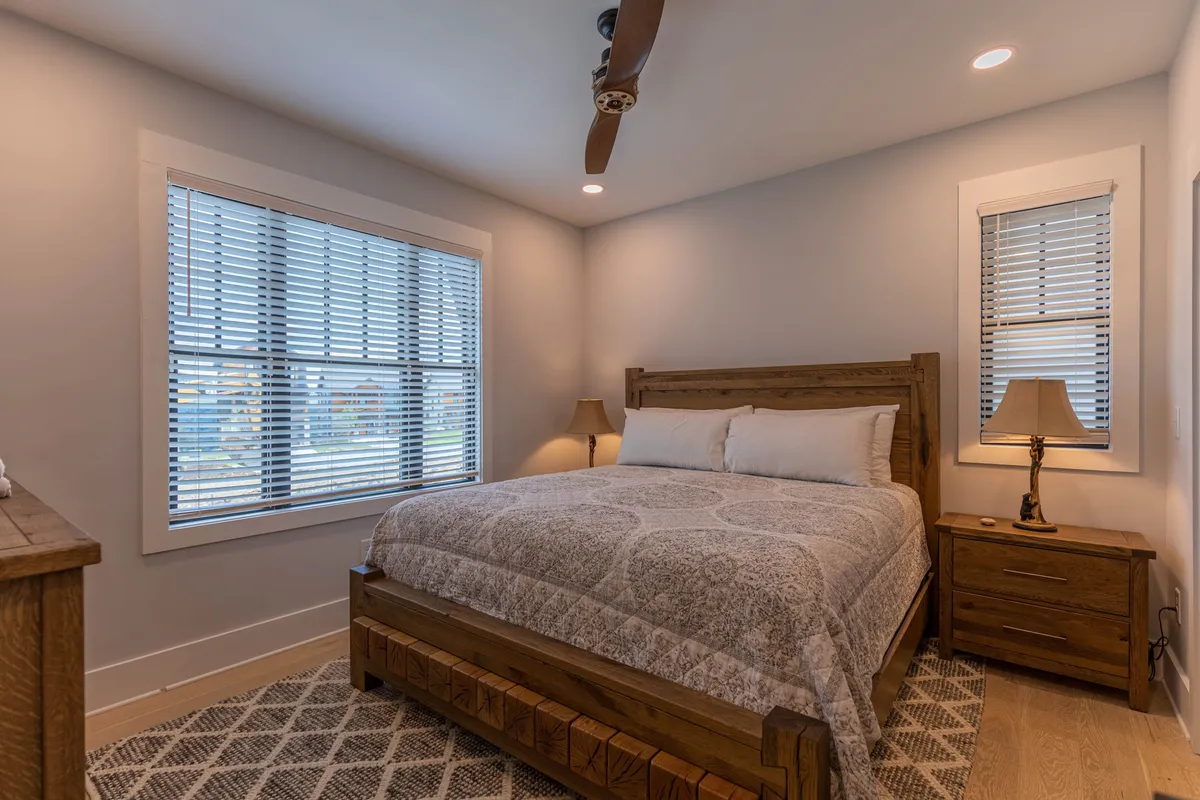 This image features a tranquil bedroom with a comfortable bed, nightstands, windows letting in natural light, and soft lighting throughout the space. The relaxed mood and inviting setup highlight the room's suitability for restful sleep and quiet moments of relaxation.
