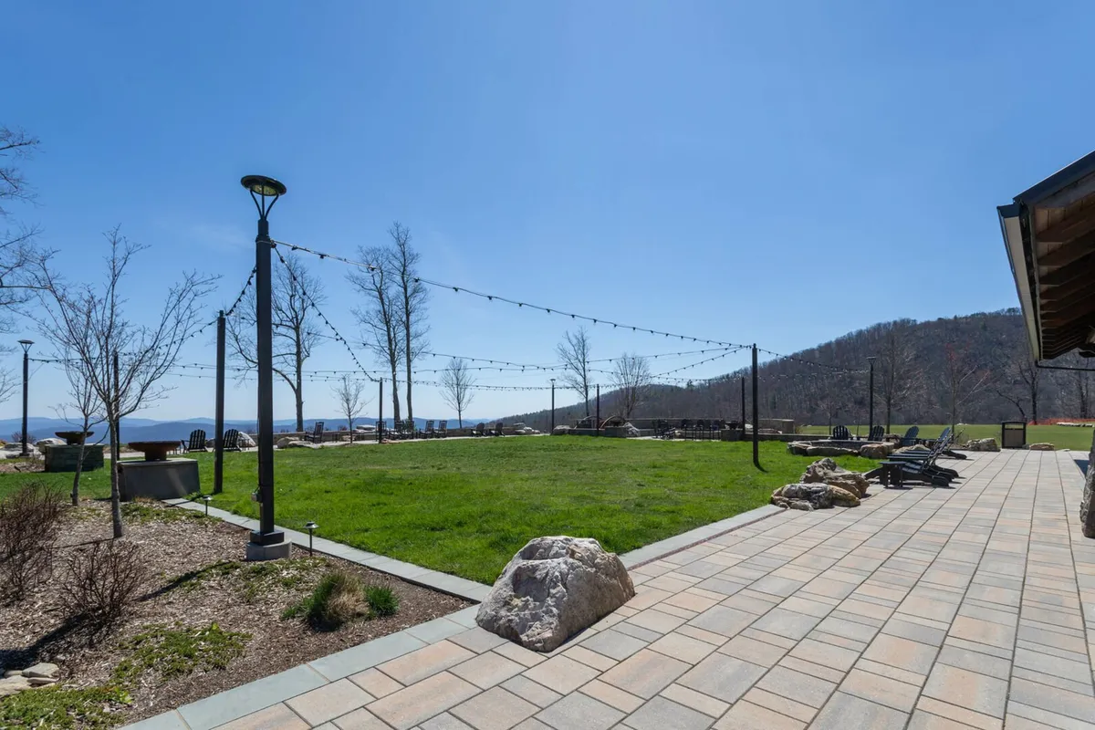 An exterior communal space featuring a green lawn, string lights, lounge chairs, patio stones, and sweeping landscape views. The setting encourages social gatherings, barbecues, and sunset viewing, while maintaining a peaceful and welcoming ambiance.